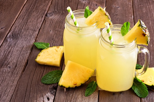 Pineapple juice in mason jar glasses on a rustic wood background