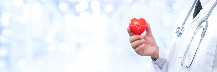 Professional medical doctor holding a red heart ball on blur office in the hospital and bokeh background. Concept of health care.