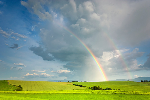 Double rainbow on a gray sky after rain. A rare atmospheric phenomenon after a storm. Beautiful hilly landscape with a real rainbow after rain on a summer day.