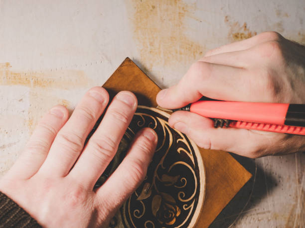 istock Close up hands of unrecognizable leather craftsman working on measurements in patterns in local workshop studio. Small business. Brown fancy tooled floral texture for background 955201496