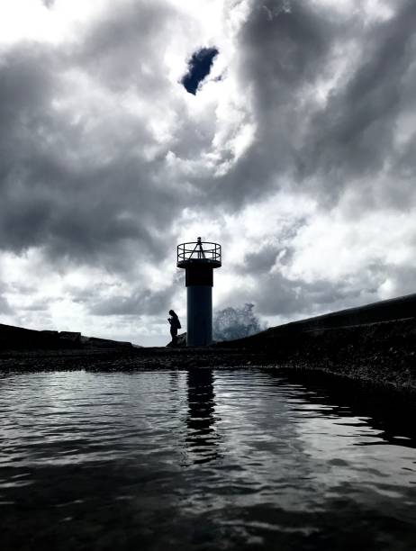 istock Dramatic storm gathering over lighthouse with wave breaking and silhouette of person 955222212