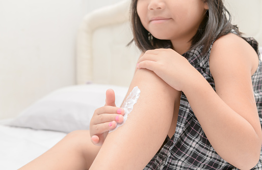 cute little girl applying  body lotion cream on her leg after shower, Selective focus Healthcare and Skin care concept.