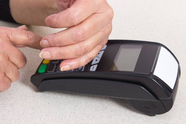 Senior woman covering hands whilst entering personal identification number on payment terminal stock photo