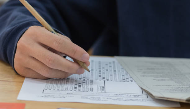 istock high school or university student hands taking exams, writing examination on paper answer sheet optical form of standardized test on desk doing final exam in classroom. Education  literacy concept. 955255960