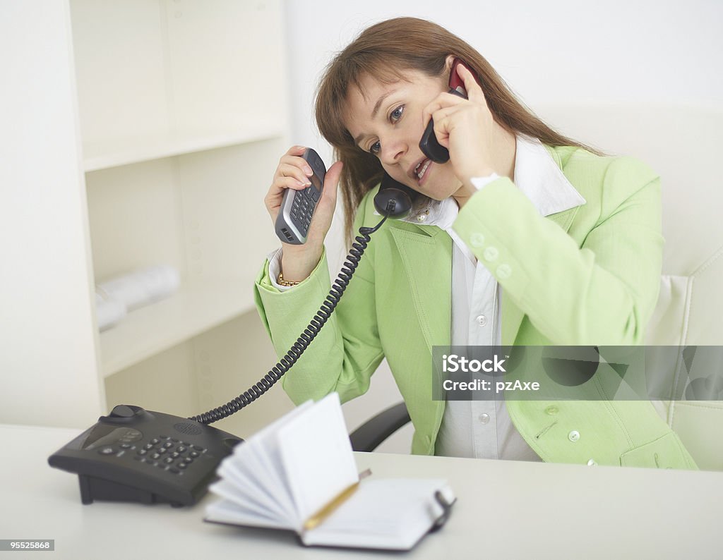 Young woman - secretary speaks by several phones simultaneously  Adult Stock Photo