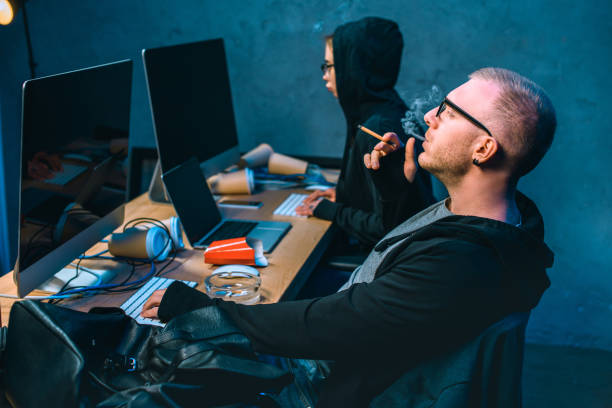 istock male hacker working on malware with accomplice and smoking 955259560