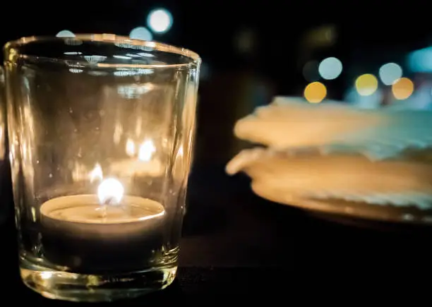 Closeup of a tealight candle burning in shot glass. Shallow depth of field. Low ambient light image.