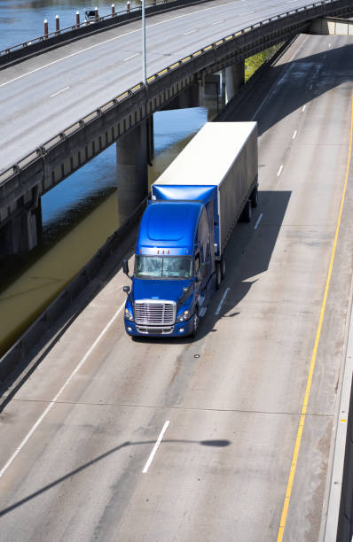 istock Big rig blue semi truck transporting covered semi trailer on turning overpass road intersection 955268528