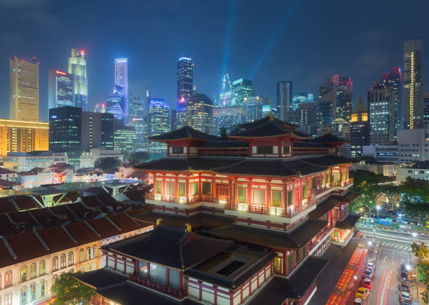 il tempio della reliquia del dente di buddha di notte a singapore chinatown, con lo skyline della città sullo sfondo. - temple singapore city singapore buddhism foto e immagini stock