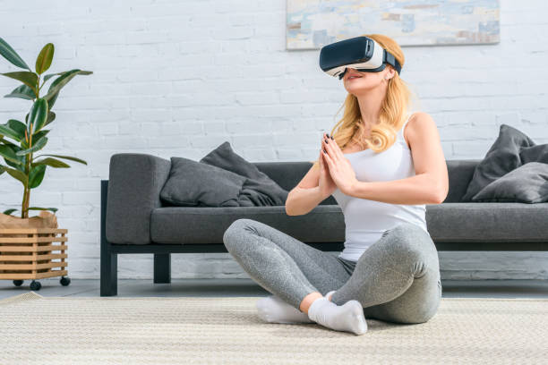 istock Young woman practicing yoga in lotus position and using virtual reality headset 955273790