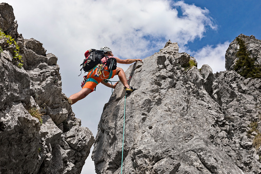 Young man using rope while climbing on vertical cliff rock wall