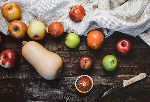 top view of pumpkin, apples, blood oranges, kitchen towel and knife on wooden table