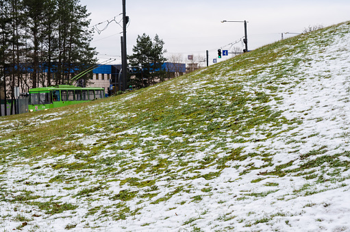 Hill partially covered in snow. Kaunas, Lithuania. A green trolleybus is also on scene.