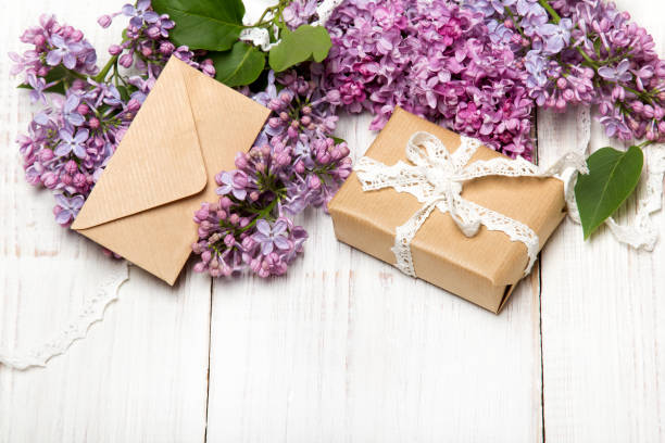 istock Lilac flowres, gift box and envelope on white wooden background. Retro style. Holiday composition, copy space 955379976