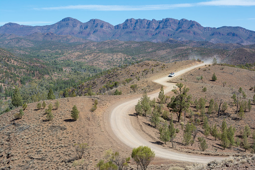 Ikara-Flinders Ranges, South Australia, Australia: March 15, 2018 - White vehicle kicking up dust on the Bunyeroo Gorge road as seen  from the Razorback lookout within the National Park