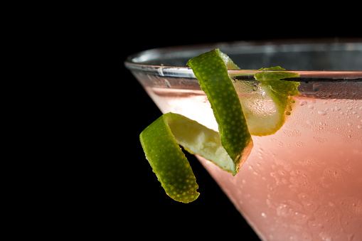 lime twist on the rim of a martini glass used as a garnish isolated on a black background
