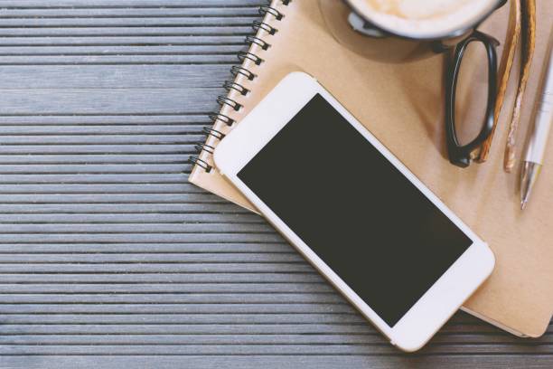 istock mobile smart phone display black screen on office desk table with book notepad,equipment supplies in the work and coffee cup. Top view with copy space. concept to work in a modern office. 955430558