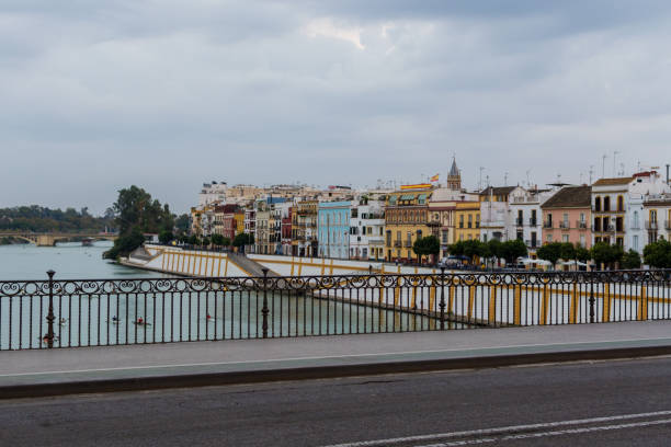 Seville, Spain - January 21, 2025: A tourboat moves in the Guadalquivir River by the Triana Bridge or Bridge of Isabel II.