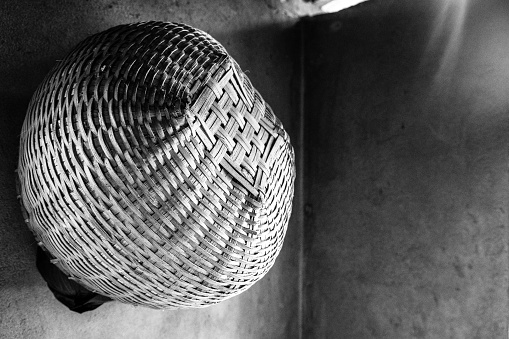 A black and white, push process filtered view of a handwoven spherical basket hanging against the corner of a shadowed interior wall.