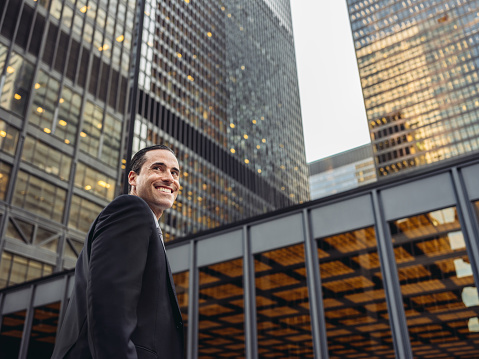 Portrait of Mid age caucasian businessman outdoors in downtown setting on the street. Tall business building with lights in the background. Happy face, looking away.