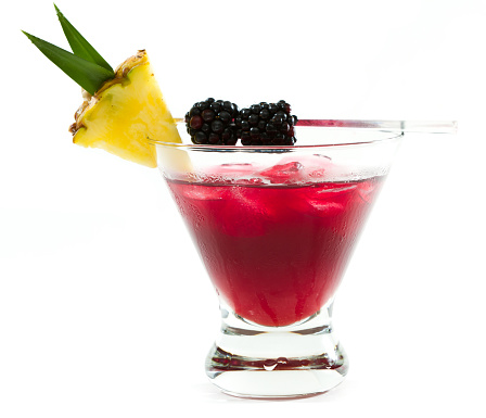 cocktail served in a stemless martini glass garnished with a pineapple slice and blackberries isolated on a white background