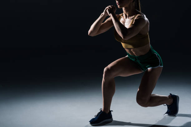 cropped view of sporty female bodybuilder doing lunges, on black cropped view of sporty female bodybuilder doing lunges, on black squatting position photos stock pictures, royalty-free photos & images