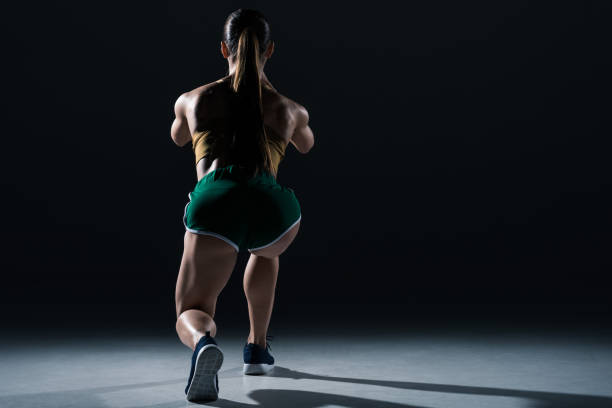 istock back view of muscular sportswoman doing lunges, on black 955454444