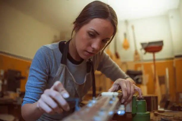 woman luthier is tuning a classical or acoustic guitar in her musical instrument workshop