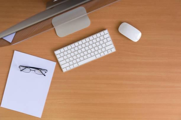 Top view all in one computer, keyboard, mouse, white paper and glasses on wooden table. flat lay style.