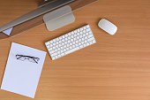 Top view all in one computer, keyboard, mouse, white paper and glasses on wooden table. flat lay style.