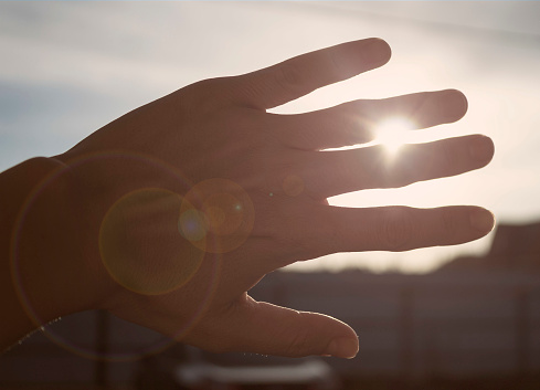 Hand obscuring the sun at sunset with rays making their way through the fingers and sun glare