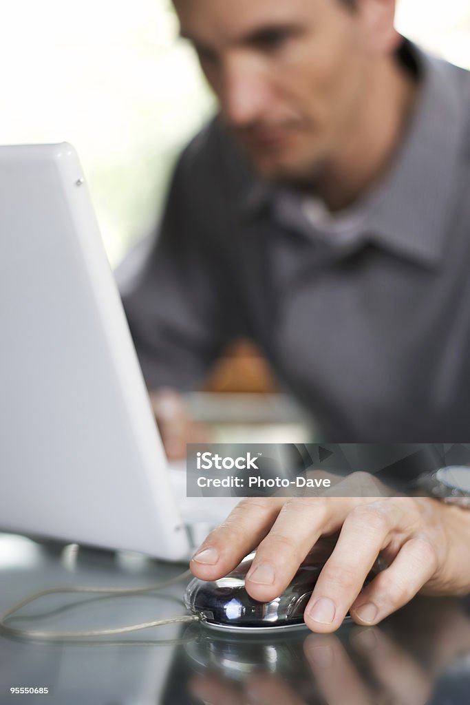 Out-of-focus man using modern computer with hand on mouse Narrow, selective focus of a man working on his laptop computer Adult Stock Photo