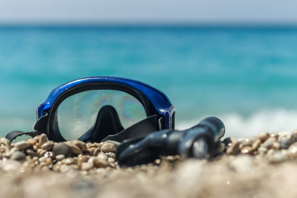 Snorkeling mask on pebble beach near splashing surfs. Active summer vacation concept with plenty of copy space for your content.