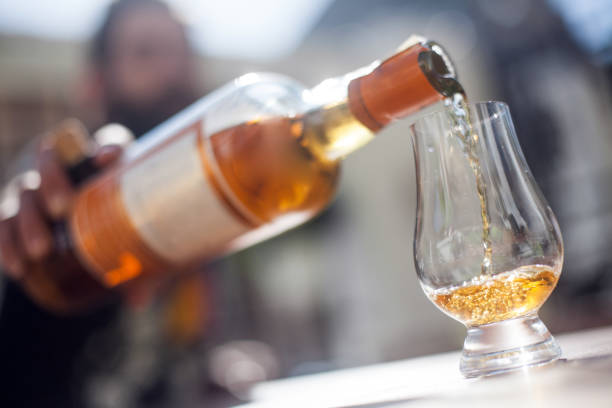 Color image of an unrecognizable man pouring whisky from a bottle into a glass.