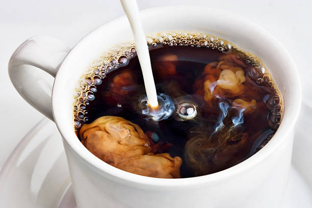 Pouring creamer into a cup of coffee stock photo