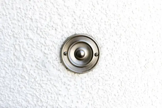 Bell button for doorbell made of stainless steel on a white wall
