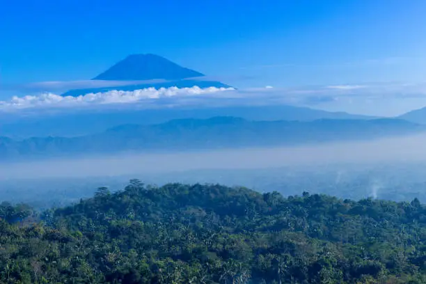 Peak of a mountain surrounded by white clouds as seen from Magelang, Indonesia.