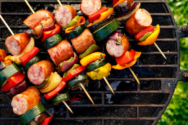 Grilled skewers of meat, sausages and various vegetables on a grill plate, outdoors, top view. Grilled skewers of meat, sausages and various vegetables on a grill plate, outdoors, top view. Grilled food, bbq shish kebab stock pictures, royalty-free photos & images