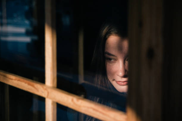 istock Smiling Young Woman Looking Through Window 955556298