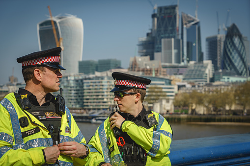 London, UK - April, 2018. Two police officers patrolling Tower Bridge during the London Marathon with the City financial district on the background. Landscape format.