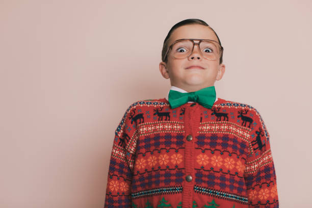 Christmas Sweater Boy with eyeglasses and an ugly sweater makes a cheesy and goofy smile at the camera. He loves giving and getting presents at Christmas. He enjoys wearing his Christmas sweater for photos.