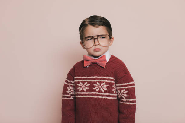 Young Ugly Christmas Sweater Boy is Sad Young Christmas sweater boy with eyeglasses and an ugly sweater makes a frown and looks away from the camera. He is disappointed because he cannot open his gifts and presents at the party. He does not want to go to the Christmas holiday party because it is boring. nerd sweater stock pictures, royalty-free photos & images