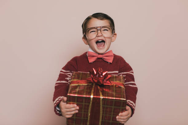 Young Christmas Sweater Boy Laughs with Gift Young Christmas sweater boy with eyeglasses and an ugly sweater is laughing at the camera. He loves getting presents from Santa at Christmas. He enjoys the excitement and happiness that comes with the holidays. christmas ugliness sweater nerd stock pictures, royalty-free photos & images