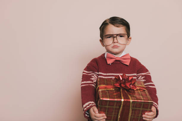Young Christmas Sweater Boy with Gift Young Christmas sweater boy with eyeglasses and an ugly sweater holds his present and makes a frown at the camera.  He is disappointed because he cannot open his gifts. He does not want to go to the Christmas holiday party because it is boring. christmas ugliness sweater nerd stock pictures, royalty-free photos & images