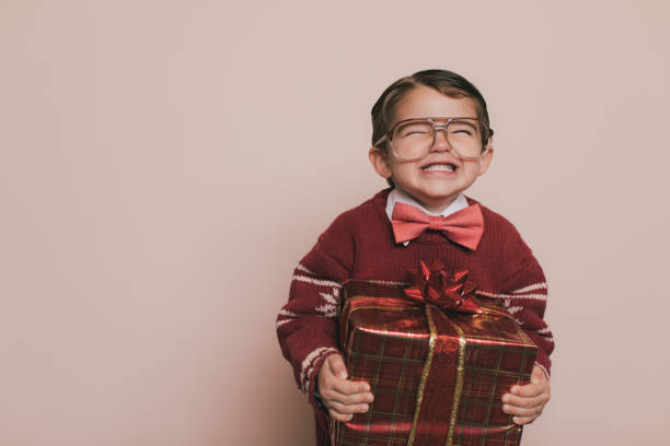 Young Christmas Sweater Boy Smiles with Gift Young Christmas sweater boy with eyeglasses and an ugly sweater is laughing at the camera. He loves getting presents from Santa at Christmas. He enjoys the excitement and happiness that comes with the holidays. birthday present photos stock pictures, royalty-free photos & images