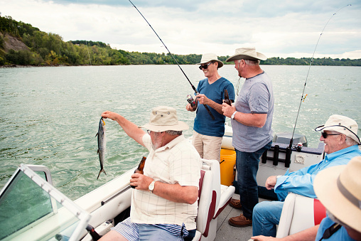 Active seniors brothers on a week-end fishing trip on the St. Lawrence River in Quebec Canada. They are happy to be together. We feel the fraternity that unites them. They also do a lot of humor. They all wear fishing hats. They are between 65 and 80 years old.