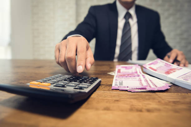 Businessman calculating the conversion rate for the indian rupee money Businessman pressing calculator calculating the conversion rate of Indian Rupee money as a return of financial invesment at the table in his office capital budget pictures stock pictures, royalty-free photos & images