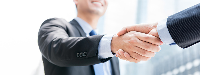 Smiling businessman making handshake with his partner outdoors in the city, panoramic web banner