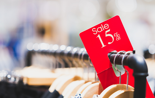 Red sale sign 15% discount on clothing rack in modern shopping mall or department store with copy space. Retail shop promotional event, new product discount, or business marketing advertising concept