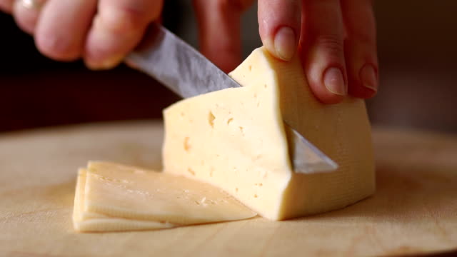 A woman cuts cheese on a cutting Board, close-up.